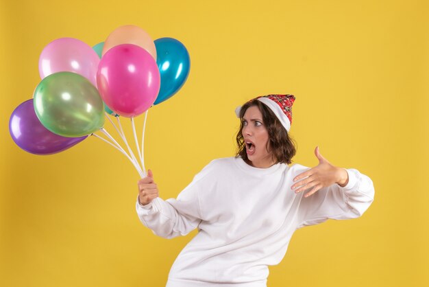 Vue de face jeune jolie femme tenant des ballons colorés sur la couleur de la femme de Noël émotion nouvel an jaune