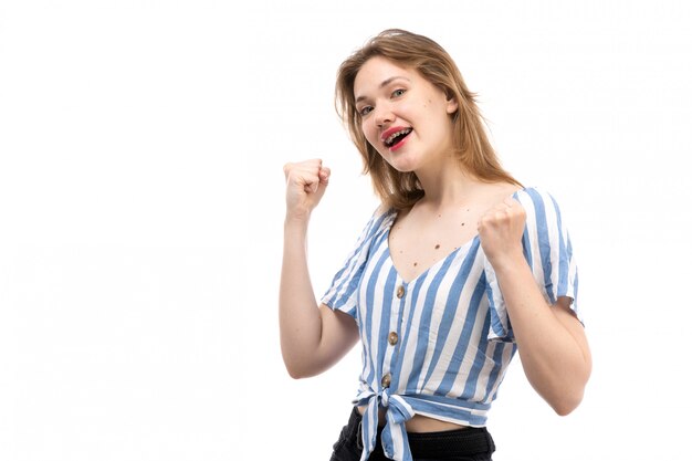 Une vue de face jeune jolie fille en t-shirt rayé bleu-blanc portant un jean noir posant à moitié souriant sur le blanc