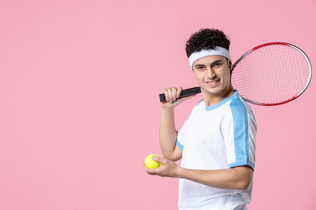 Vue de face jeune joueur de tennis en raquette de vêtements de sport sur mur rose