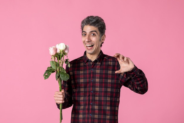 Photo gratuite vue de face jeune mâle avec de belles roses roses sur mur rose