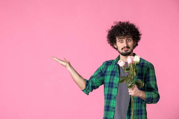 Photo gratuite vue de face jeune mâle avec des roses roses sur rose