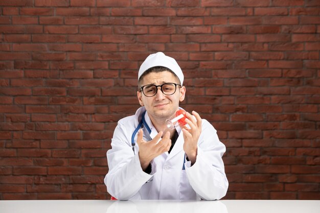 Vue de face jeune médecin en costume médical blanc tenant une petite fiole vide