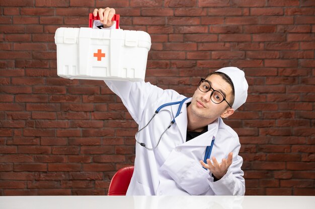 Vue de face jeune médecin en costume médical blanc avec trousse de premiers soins