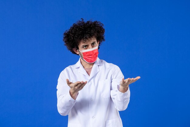 Vue de face jeune médecin en costume médical avec masque rouge sur fond bleu médicament covid- virus pandémique médecine vaccin santé