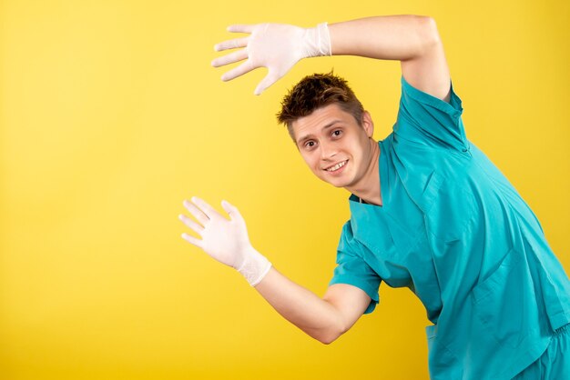 Vue de face jeune médecin de sexe masculin en costume médical avec des gants sur fond jaune