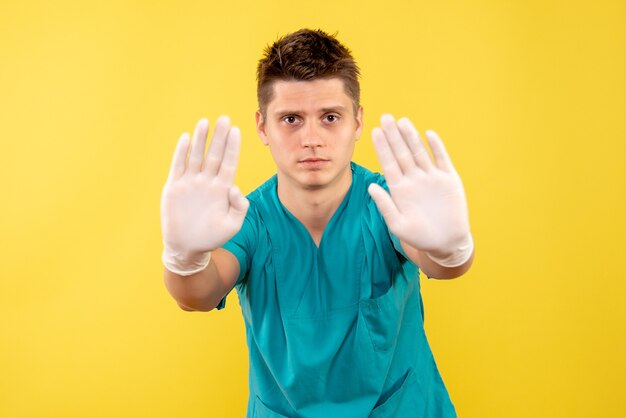 Vue de face jeune médecin de sexe masculin en costume médical portant des gants sur fond jaune