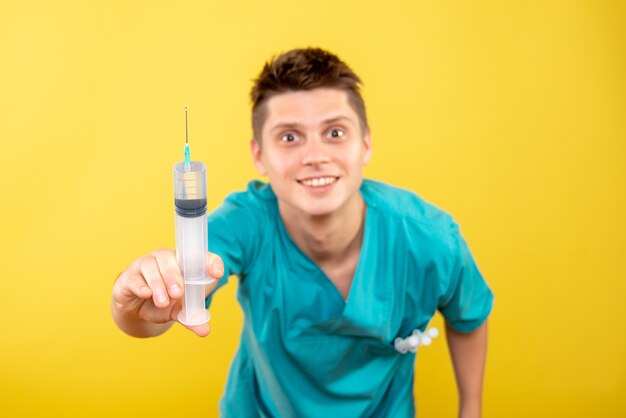 Vue de face jeune médecin de sexe masculin en costume médical tenant injection sur fond jaune