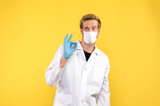Vue de face jeune médecin de sexe masculin sur fond jaune maladie médicale pandémique covid
