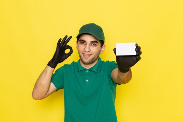 Vue de face jeune messager en chemise verte casquette verte tenant une carte blanche sur jaune