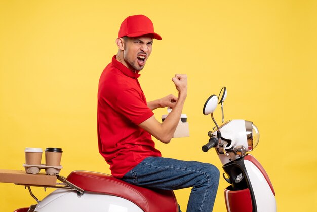 Vue de face jeune messager en uniforme rouge avec du café sur fond jaune