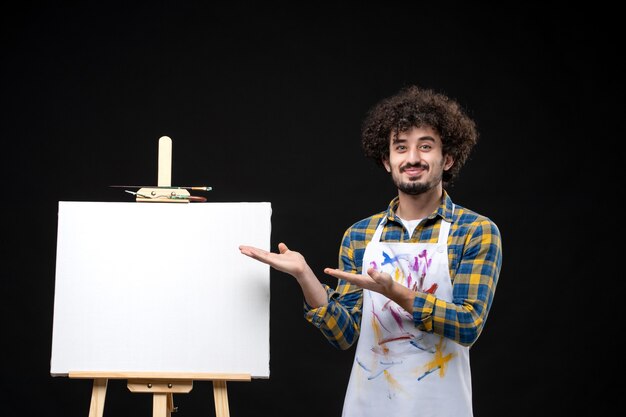 Vue de face jeune peintre masculin avec chevalet pour dessiner sur un tableau noir