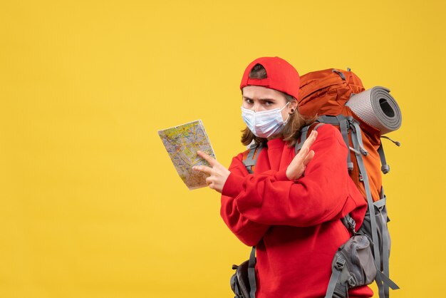 Vue de face jeune randonneuse avec sac à dos et masque tenant la carte, croisement