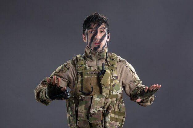 Vue de face jeune soldat se rendant en camouflage avec un pistolet sur un mur sombre