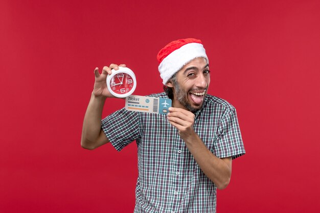 Vue de face jeune tenant un billet et une horloge sur le mur rouge temps des émotions masculines rouges