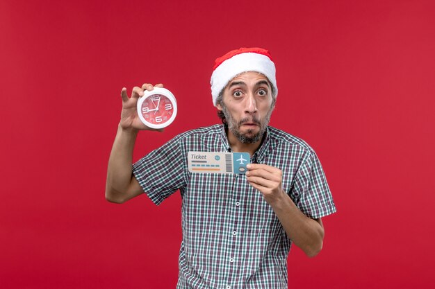 Vue de face jeune tenant une horloge et un billet sur le mur rouge de temps d'émotion rouge mâle