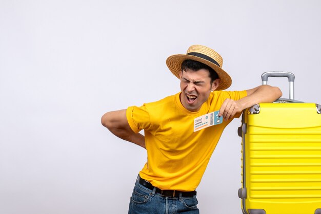 Vue de face jeune touriste debout près de valise jaune tenant son dos avec douleur