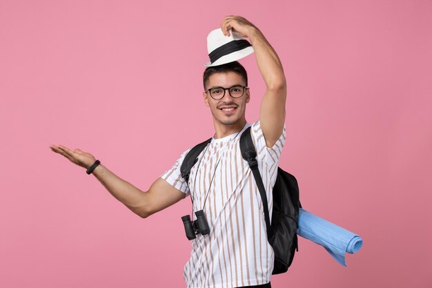 Vue de face jeune touriste masculin enlevant son chapeau sur un bureau rose