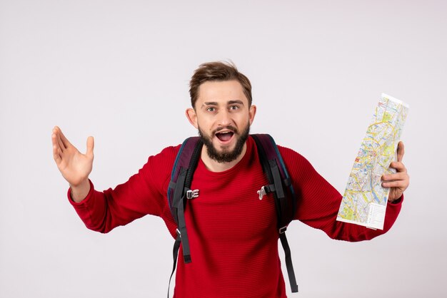 Photo gratuite vue de face jeune touriste masculin avec sac à dos explorant la carte sur le mur blanc avion covid vacances émotion virus vol couleurs