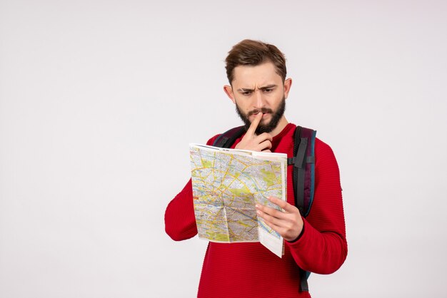 Vue de face jeune touriste masculin avec sac à dos explorant la carte sur le mur blanc ville vacances émotion route tourisme couleur humaine