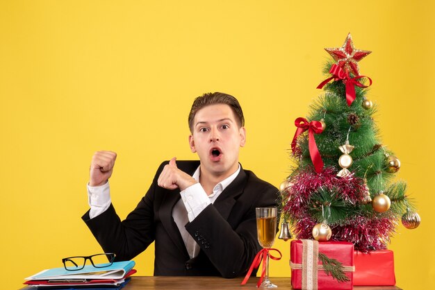 Vue de face jeune travailleur masculin assis avec des cadeaux de Noël et arbre