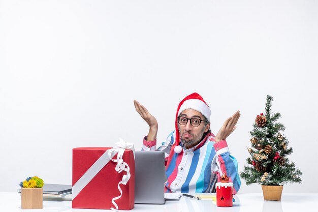 Vue de face jeune travailleur masculin assis dans son lieu de travail sur fond blanc