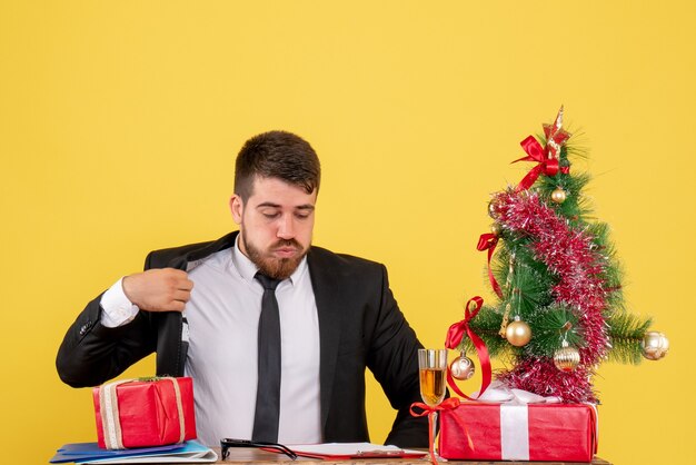 Vue de face jeune travailleur masculin assis derrière son lieu de travail sur jaune