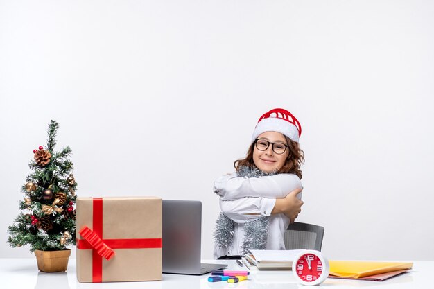 Vue de face jeune travailleuse assise devant son lieu de travail souriant sur fond blanc