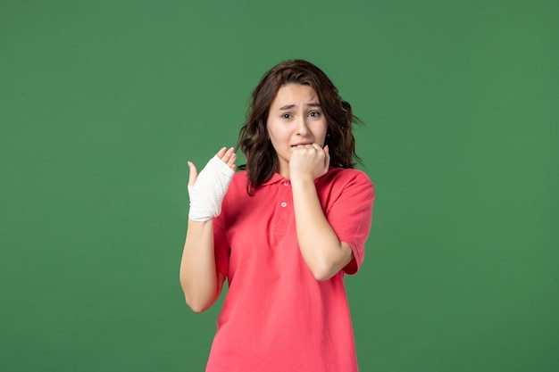 Vue de face jeune vendeuse avec un bandage sur sa main blessée sur fond vert couleur de travail uniforme blessure santé hôpital shopping travail cri