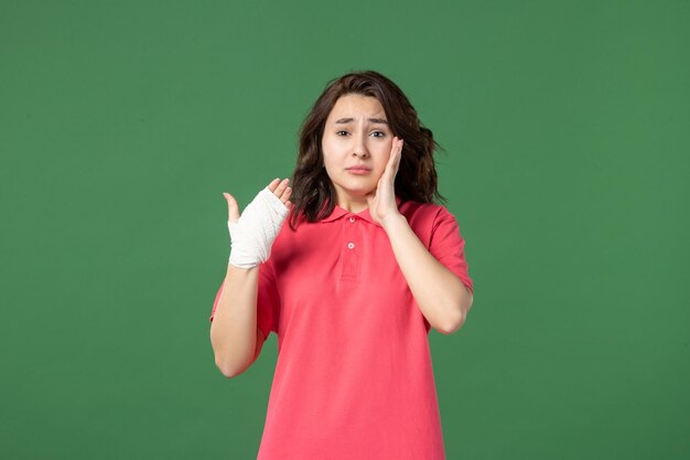 Vue de face jeune vendeuse avec un bandage sur sa main blessée sur une surface verte