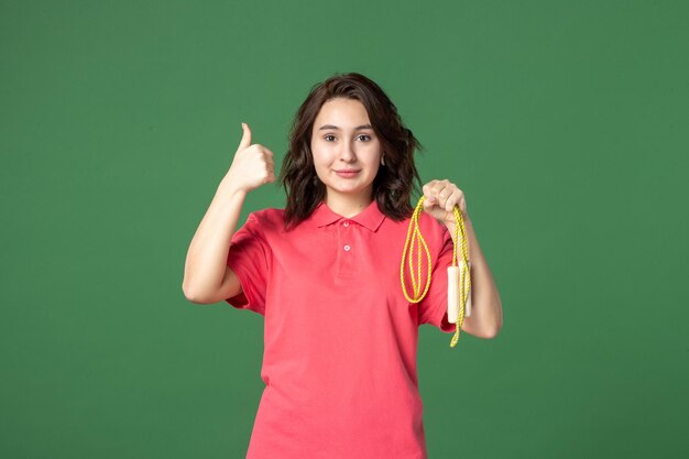 Vue de face jeune vendeuse tenant une corde à sauter sur fond vert sport vente boutique uniforme shopping travailleur travail présent