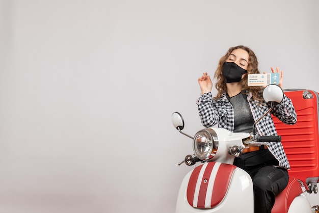 Vue de face jeune voyageur avec masque noir sur cyclomoteur tenant un billet de voyage fermant les yeux