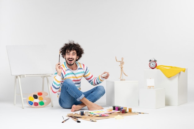 Vue de face de jeunes hommes dessinant des images avec des peintures sur un mur blanc