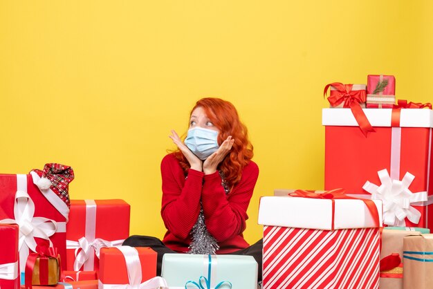 Vue de face jolie femme assise autour de cadeaux en masque sur jaune