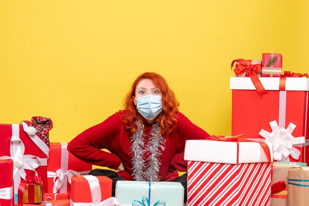 Vue de face jolie femme assise autour de cadeaux en masque sur jaune