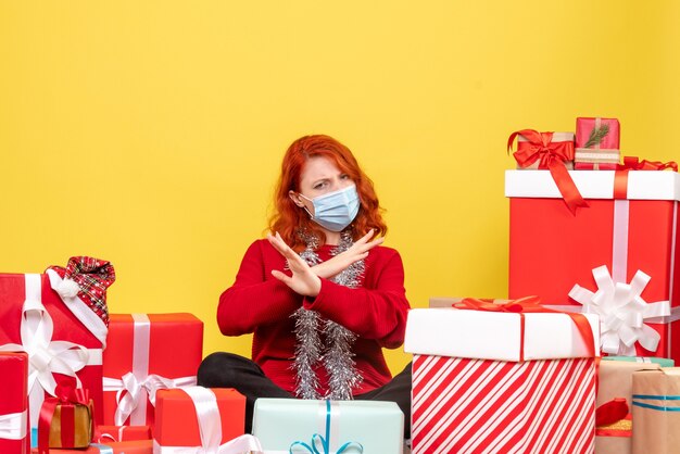 Vue de face jolie femme assise autour de cadeaux en masque sur jaune