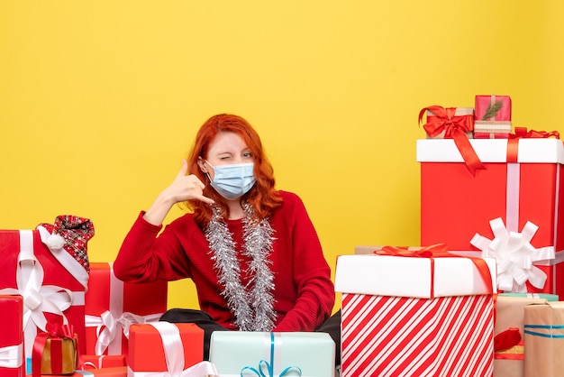 Vue de face jolie femme assise autour de cadeaux en masque sur jaune