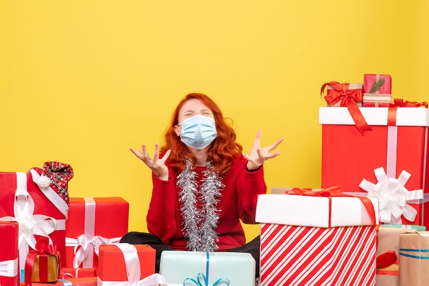 Vue de face jolie femme assise autour de cadeaux en masque sur jaune