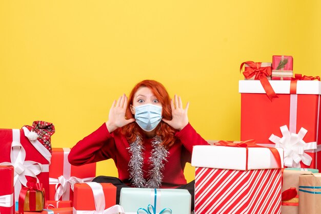 Vue de face jolie femme assise autour de cadeaux en masque sur jaune