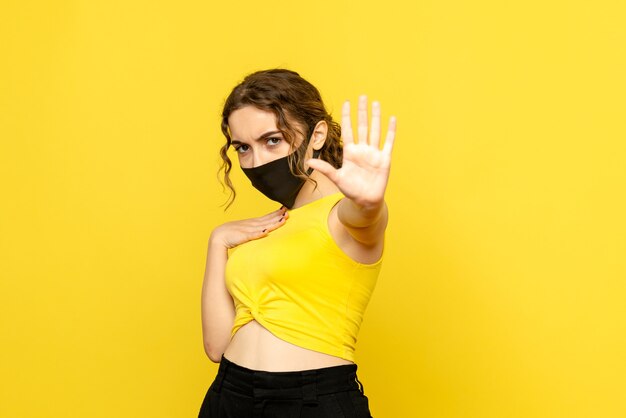 Vue de face de la jolie femme au masque noir sur jaune