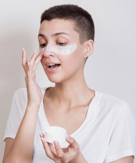 Vue de face, jolie femme aux cheveux courts avec une crème pour la peau