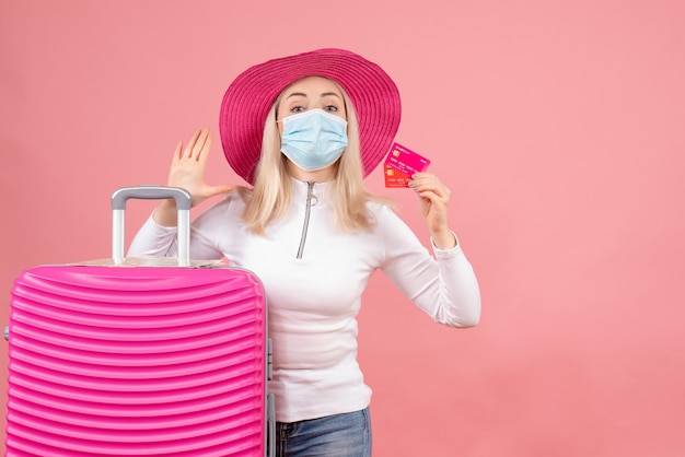 Vue de face jolie femme blonde avec masque debout près de cartes valise hlding