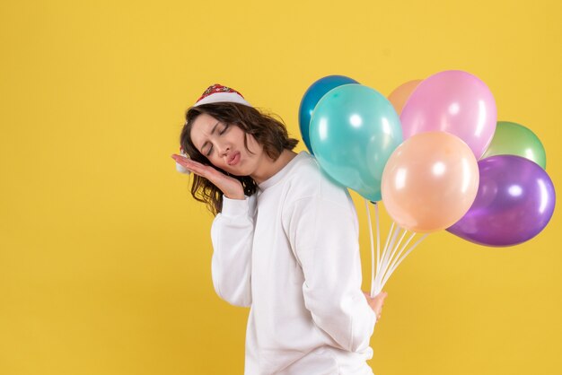 Vue de face jolie femme cachant des ballons colorés sur jaune