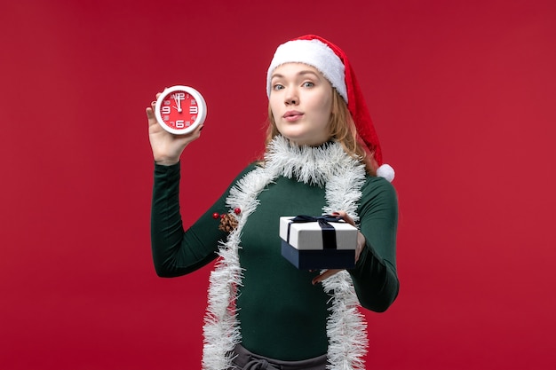 Vue de face jolie femme avec des cadeaux avec horloge sur fond rouge