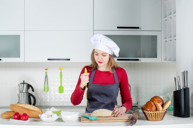 Vue de face jolie femme en chapeau de cuisinier et tablier brandissant un couteau