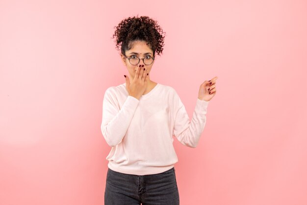 Vue de face de jolie femme couvrant sa bouche sur un mur rose