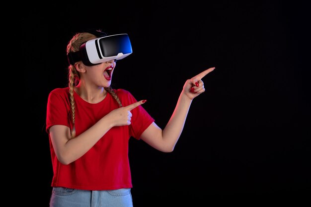 Vue de face d'une jolie femme jouant à la réalité virtuelle sur une fantaisie de jeu à ultrasons sombre