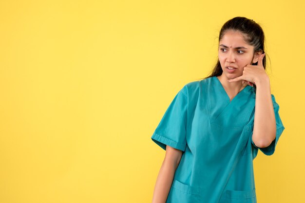 Vue de face de la jolie femme médecin faisant appelez-moi geste phne sur mur jaune