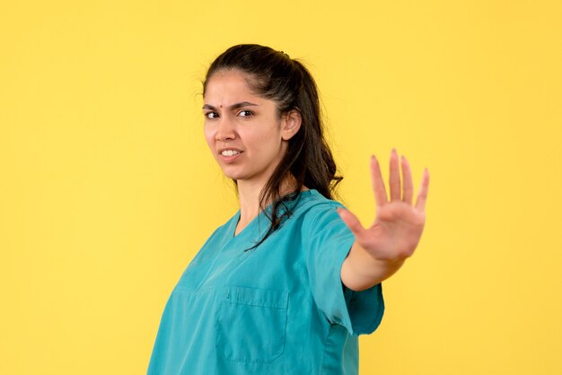 Vue de face de la jolie femme médecin faisant panneau d'arrêt sur mur jaune