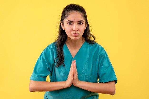 Vue de face de la jolie femme médecin joignant ses mains sur un mur jaune