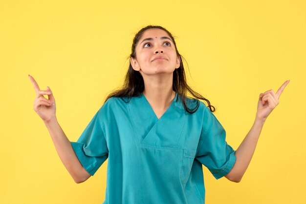 Vue de face de la jolie femme médecin à la recherche debout sur le mur jaune